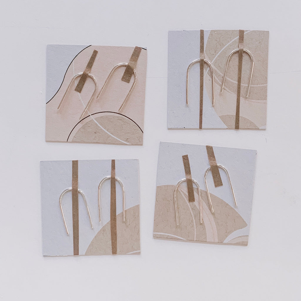Minimal arc earrings taped to recycled kraft earring cards, with a minimal geometric peach design