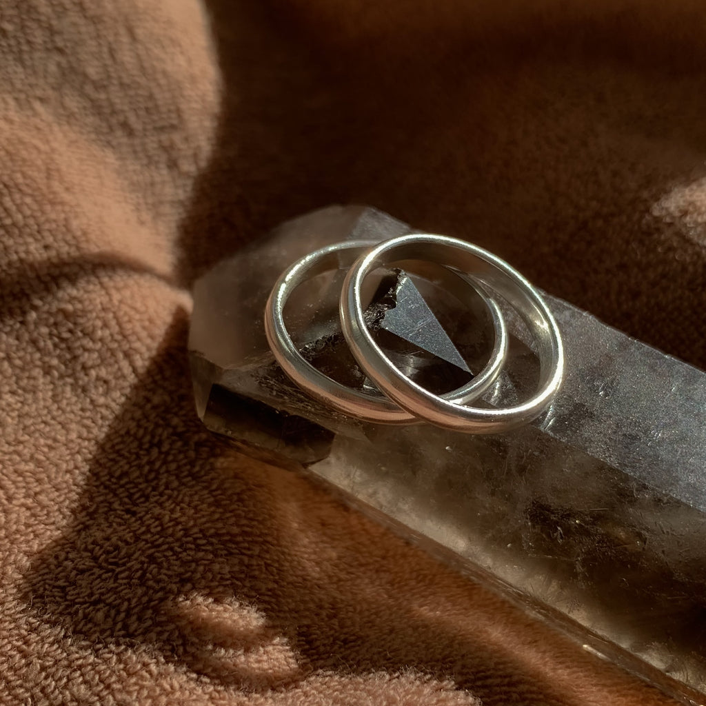A pair of silver stacking rings sunbathing on a quartz crystal, with a brown background.