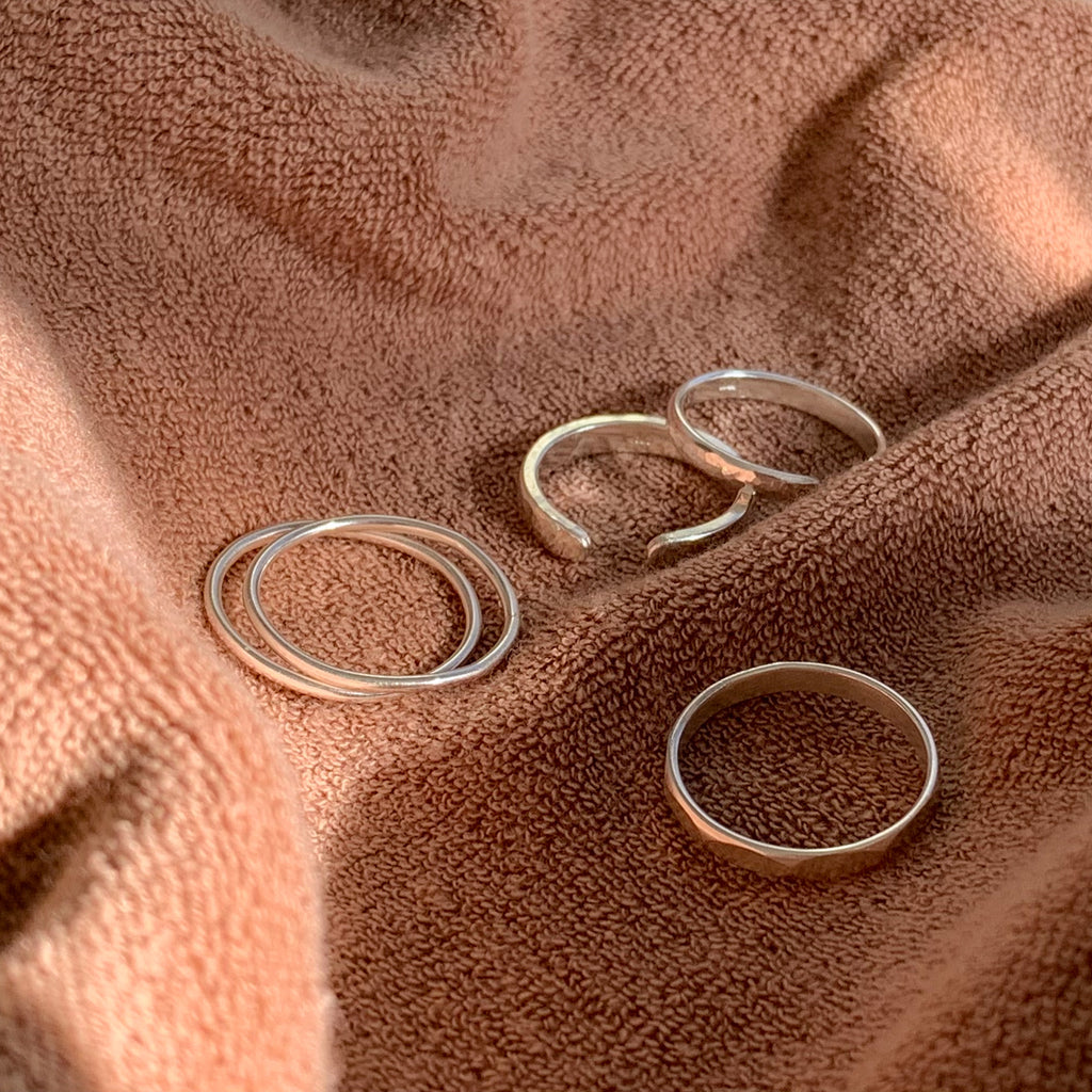 Simple silver stacking band rings on a brown cotton terry backdrop in the sunlight.