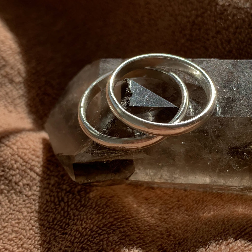 Two simple, brushed silver rings sit atop a smoky quartz crystal, shining in the sunlight.