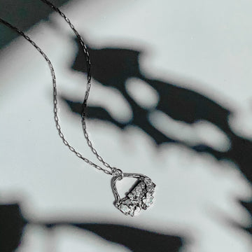 A small silver pendant on a silver layering chain. The crystal textured layering necklace is surrounded by botanical shadows. 